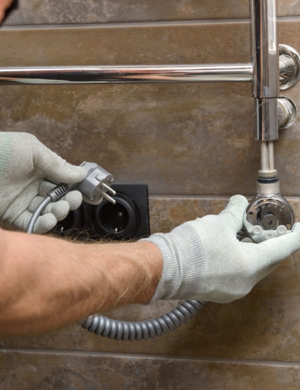 A worker is installing a heating element in the towel warmer in the bathroom.