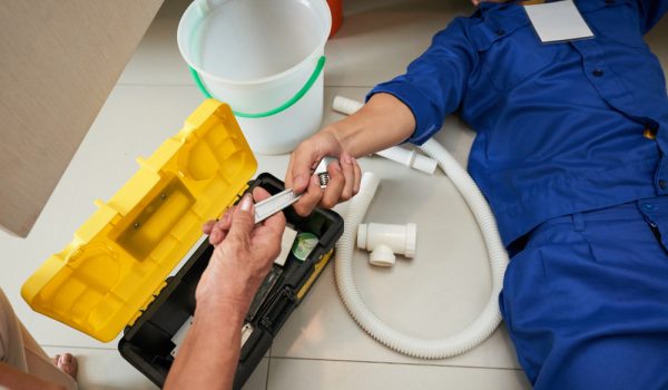 Senior woman passing wrench to plumber who is lying on the floor